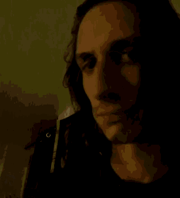 a man with long hair looks at the camera in front of a sign that says ' s '