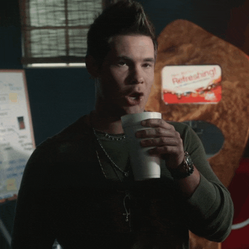 a man is drinking from a styrofoam cup in front of a refreshing sign