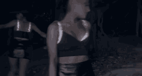 ariana grande is dancing in the dark in a black crop top and black shorts .