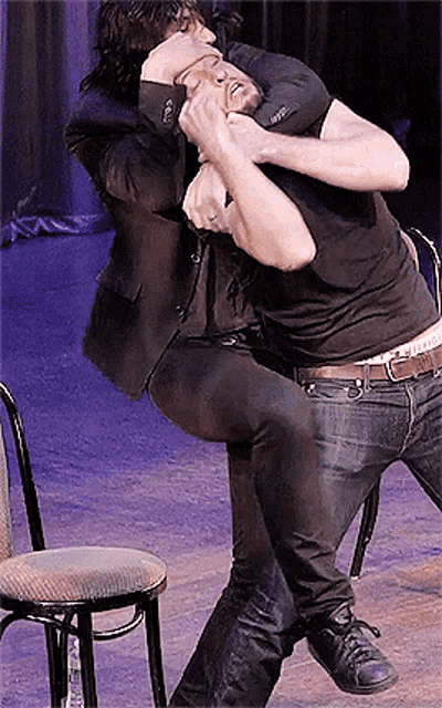 two men are wrestling on a stage and one has a belt that says ' abercrombie & fitch ' on it