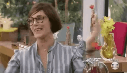 a woman wearing glasses is sitting at a table with a vase of flowers .