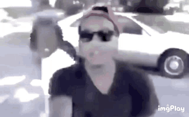 a man wearing sunglasses and a red hat is standing in front of a car .