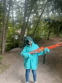 a person in a blue hoodie is holding a nerf gun in the woods