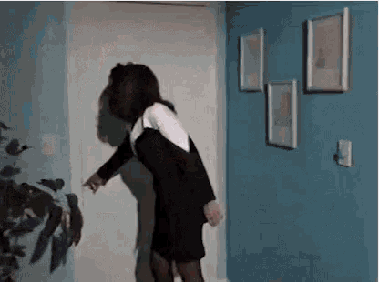 a woman in a black dress is standing in front of a door in a hallway .