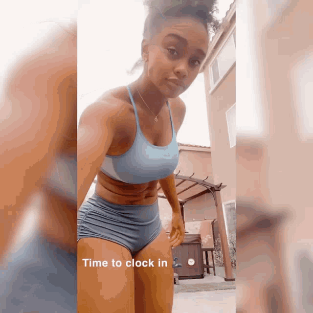 a woman in a blue sports bra and shorts is standing in front of a house and says time to clock in