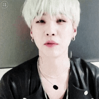 a close up of a person with white hair wearing a black jacket and a necklace .