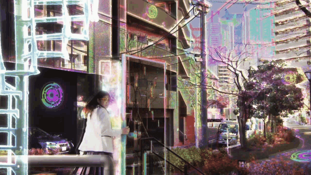 a woman in a white coat stands in front of a building with a rainbow colored wheel