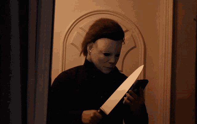 a man in a mask is holding a knife and looking at his phone