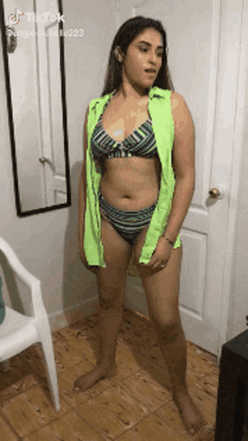 a woman in a bikini is standing in front of a mirror and a chair .