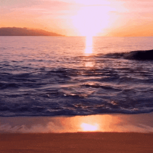 the sun is setting over the ocean with mountains in the distance