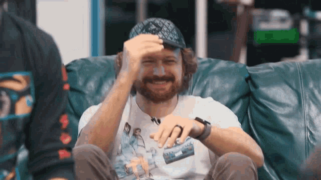 a man with a beard is sitting on a couch with his hands on his head