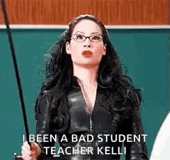 a woman in a black suit and glasses is holding a stick in front of a blackboard .