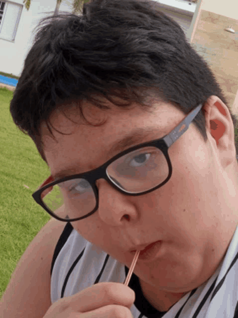 a young boy wearing glasses and a puma shirt drinks through a straw