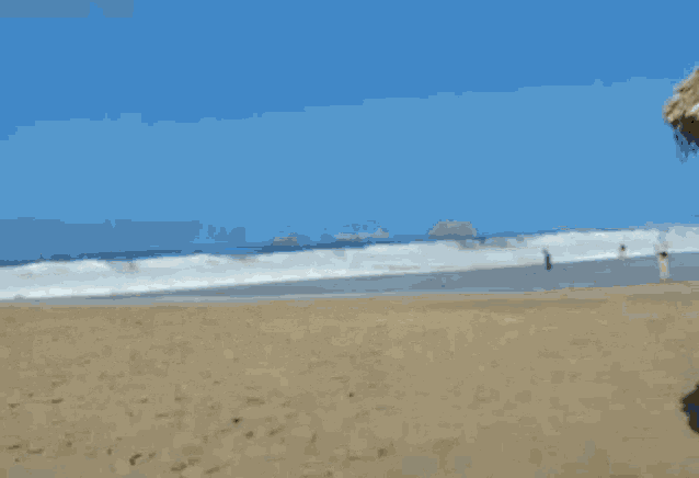 a beach with waves crashing on the sand and a blue sky