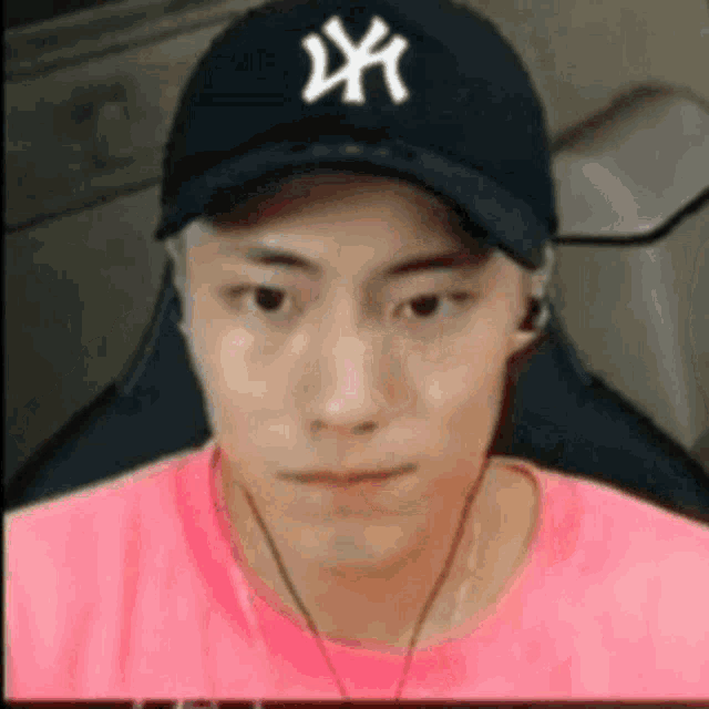 a man wearing a ny hat and a pink shirt is sitting in front of a computer .