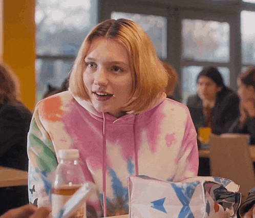 a girl wearing a tie dye sweatshirt looks surprised