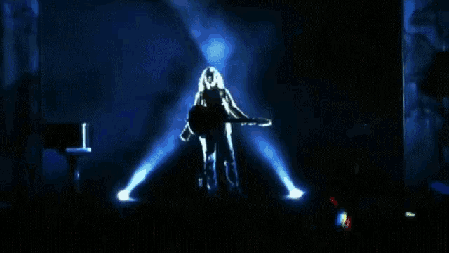 a man is playing a guitar on a stage with a piano in the background