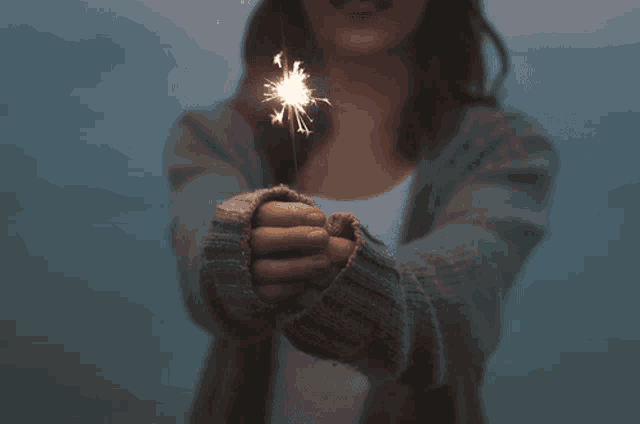 a woman in a grey sweater holds a sparkler in her hand