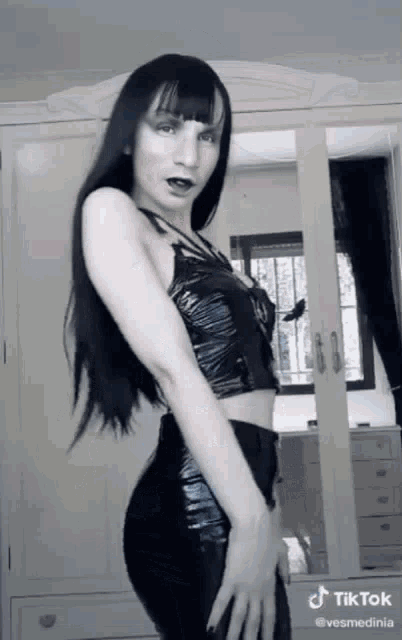 a woman in a black top and black pants is dancing in front of a mirror with tiktok written on the bottom