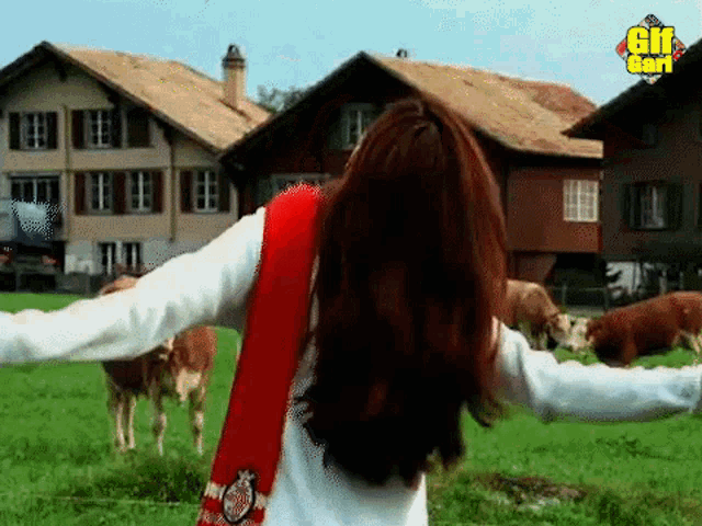 a woman is standing in a field of cows with her arms outstretched in front of a gif card logo .