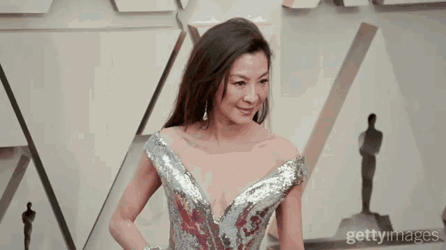 a woman in a silver sequined dress stands in front of an oscars sign