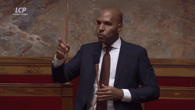 a man in a suit and tie is speaking into a microphone and says tu vas la fermer