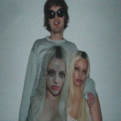 a man wearing sunglasses stands next to two women with their faces painted on their shirts