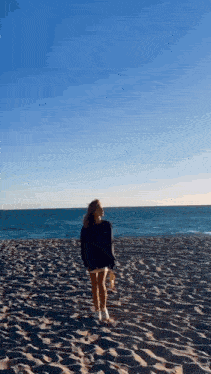 a woman is walking on a sandy beach near the ocean holding a bottle of water .