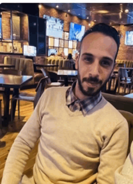a man with a beard sits in a restaurant looking at the camera