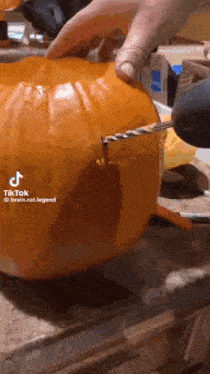 a person is using a drill to carve a pumpkin on a table