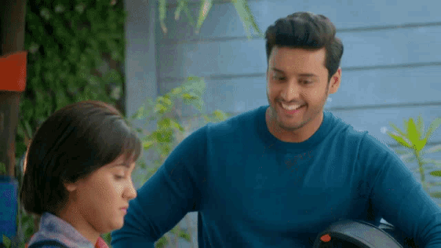 a man in a blue shirt is smiling and holding a helmet