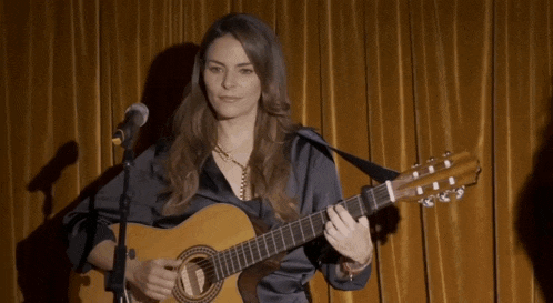 a woman singing into a microphone while holding a guitar