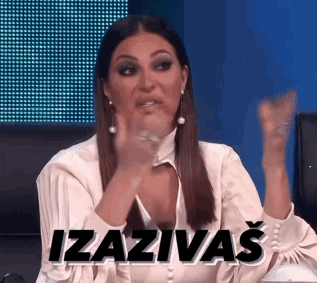 a woman in a white shirt is sitting at a table with her hands up and the word izaziva written on the screen .