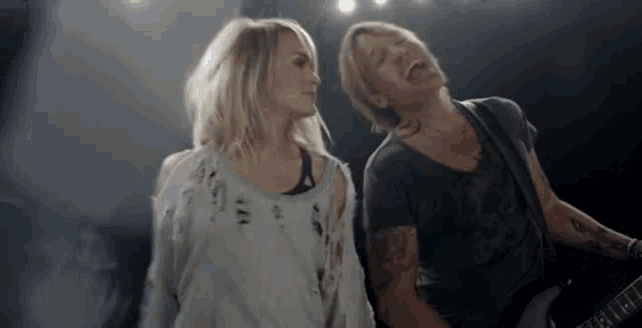 a man and a woman are standing next to each other on a stage playing guitars .