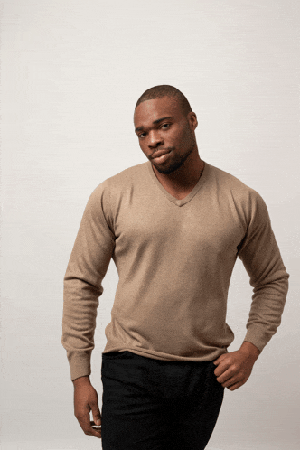 a man wearing a tan sweater and black pants is standing with his hands in his pockets