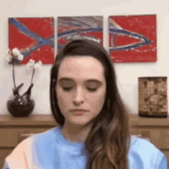 a woman with her eyes closed is sitting in front of a wall with three paintings .