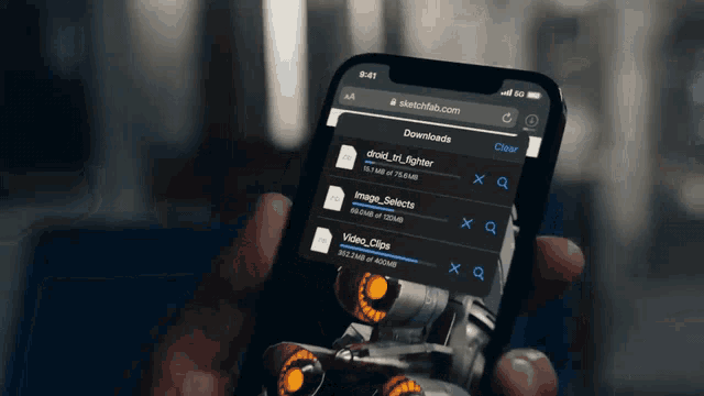 a person is holding a cell phone with sketchfab.com on it