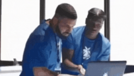 two men are sitting at a table with a laptop .