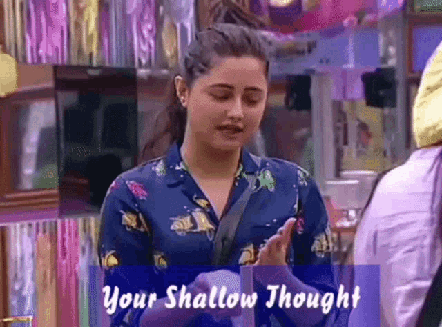 a woman in a blue shirt is standing in front of a sign that says " your shallow thought "