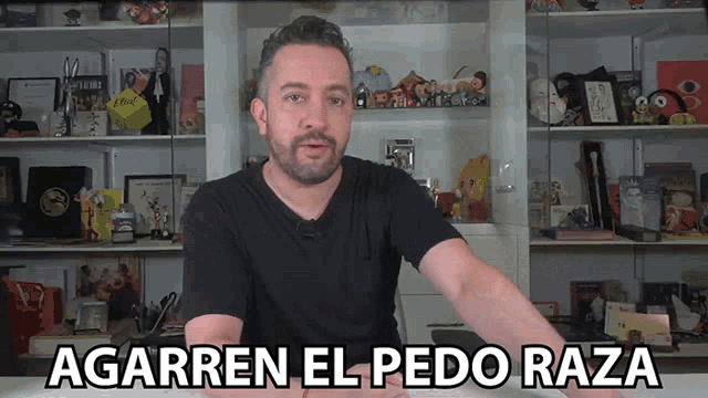 a man in a black shirt is standing in front of a shelf with a sign that says agarren el pedo raza