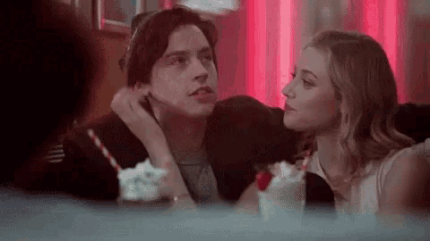 a man and a woman are sitting at a table with a milkshake and looking at each other .