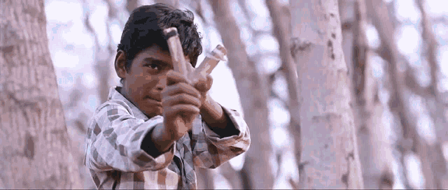 a young boy is holding a slingshot in front of a tree .
