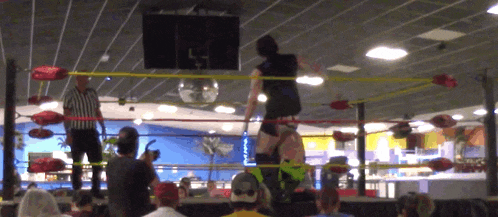 a referee stands in a wrestling ring watching a wrestler perform a move