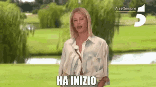 a woman is standing in front of a green field with the words ha inizio written on the ground .