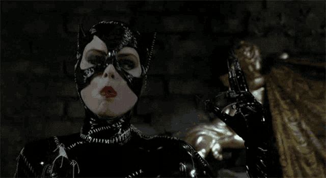 a man in a tuxedo is laying on a bed with a woman in a catsuit standing behind him