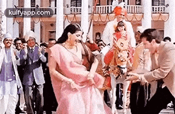 a woman in a pink sari is dancing in front of a crowd of people .