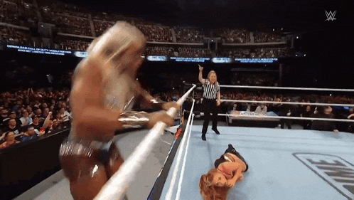 a woman is laying on the ground in a wrestling ring while a referee stands behind her