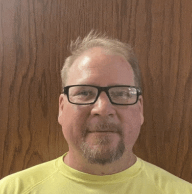 a man wearing glasses and a yellow shirt stands in front of a wooden door