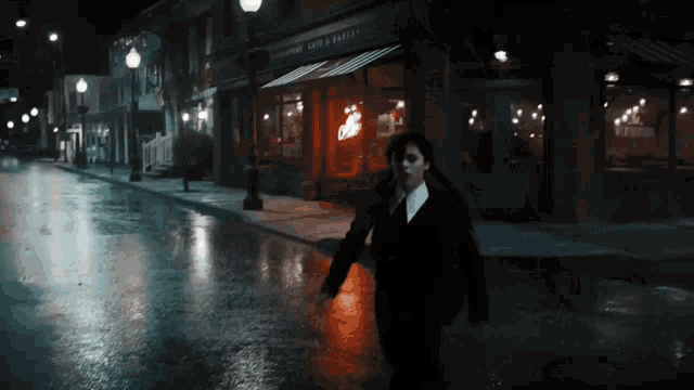 a person is walking down a wet street in front of a store called cafe & bakery