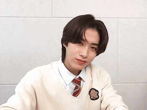 a young man wearing a white sweater and a red tie winks at the camera